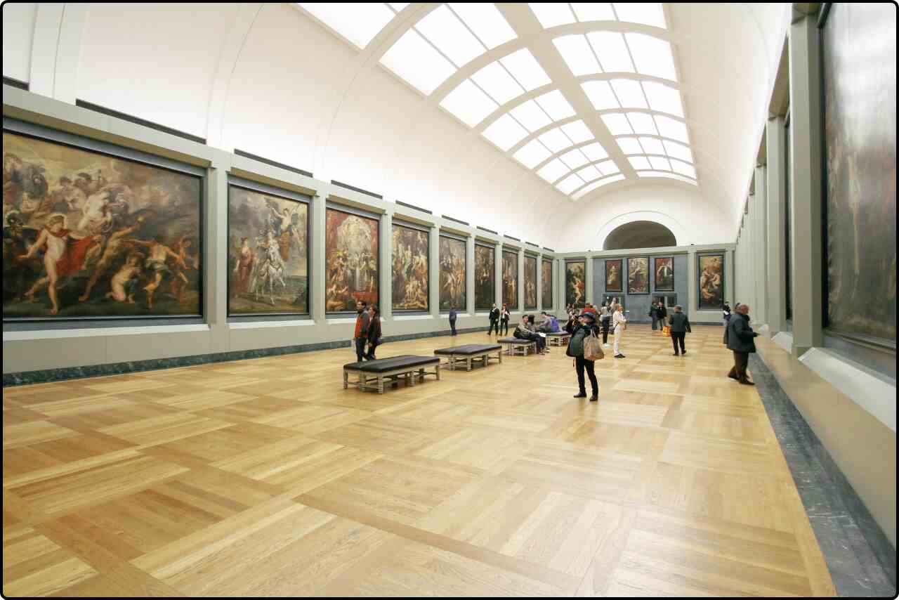 A gallery exhibit showcasing a display of paintings arranged on white walls.